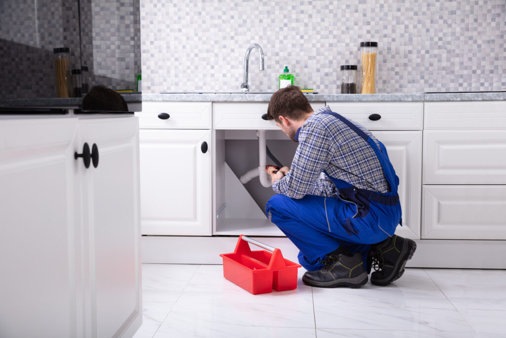 Man working plumbing underneath kitchen sink on the pipes
