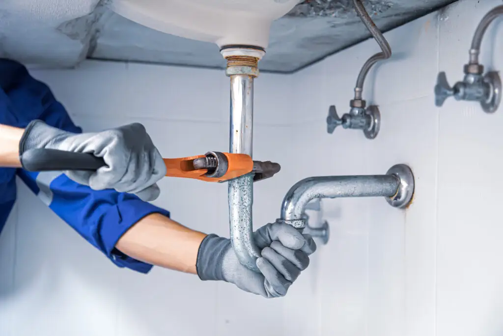 Technician plumber using a wrench to repair a water pipe under the sink. Concept of maintenance, fix water plumbing leaks, replace the kitchen sink drain, cleaning clogged pipes is dirty or rusty.