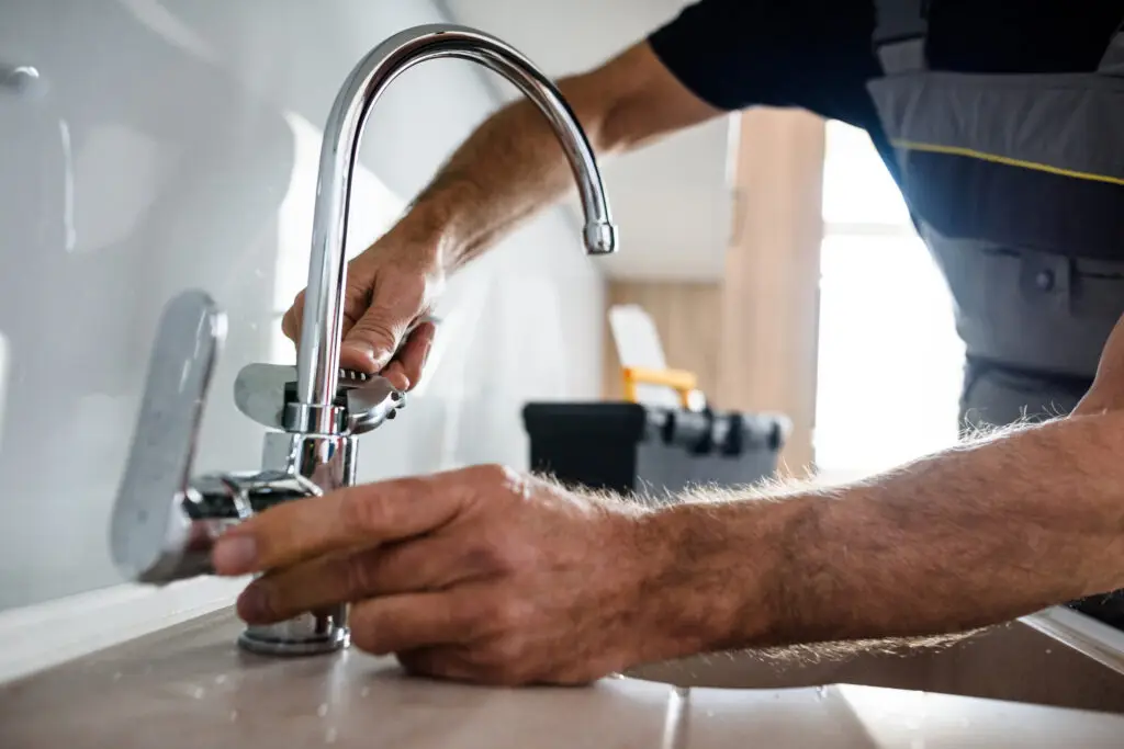 focused plumber holding metal pipe near kitchen faucet and tools on worktop