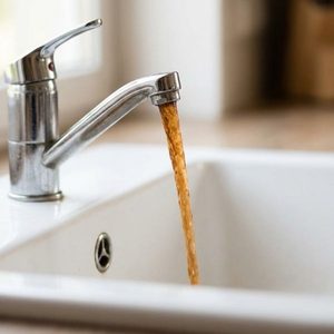 Discolored, rusty water flows from a kitchen faucet, signaling internal tank corrosion.